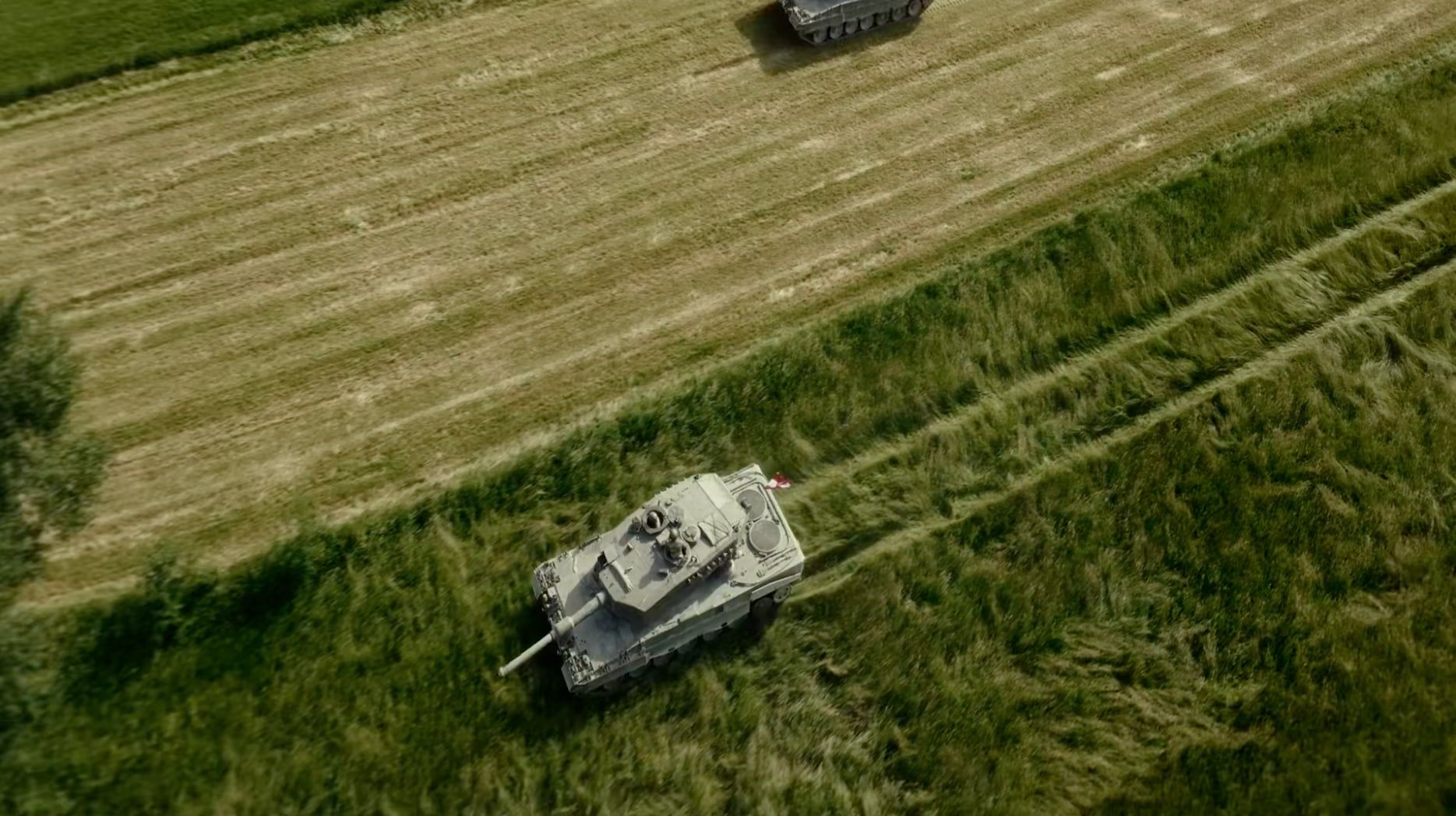 Ein Panzer des Österreichischen Bundesheeres fährt über ein grünes Feld, im Hintergrund ist ein weiteres Kettenfahrzeug zu sehen.